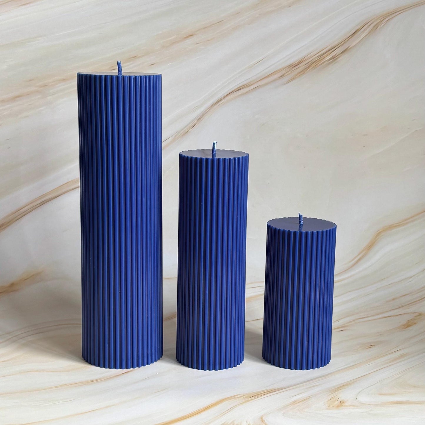 Three blue cylindrical candles are arranged in a row against a marble background.
