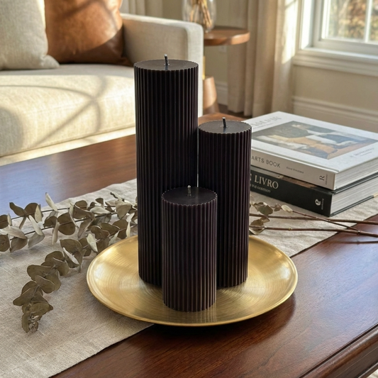 a wooden coffee table with three dark brown cylindrical candles in a gold tray, along with some greenery and a book.