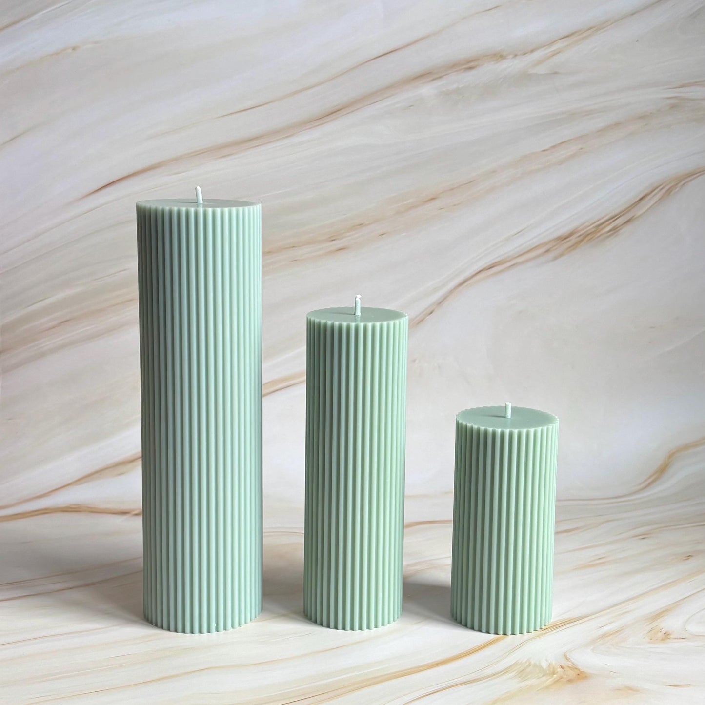 Three green cylindrical candles with vertical lines are arranged in a row against a marble-like background.