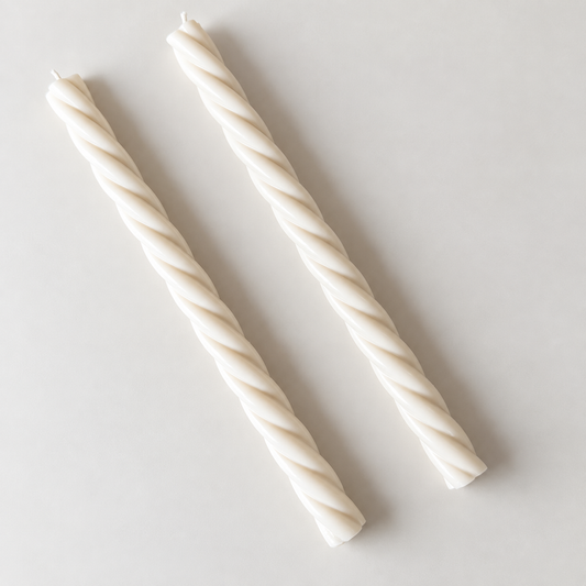Two white candles with twisted shapes are placed side by side on a plain white surface.