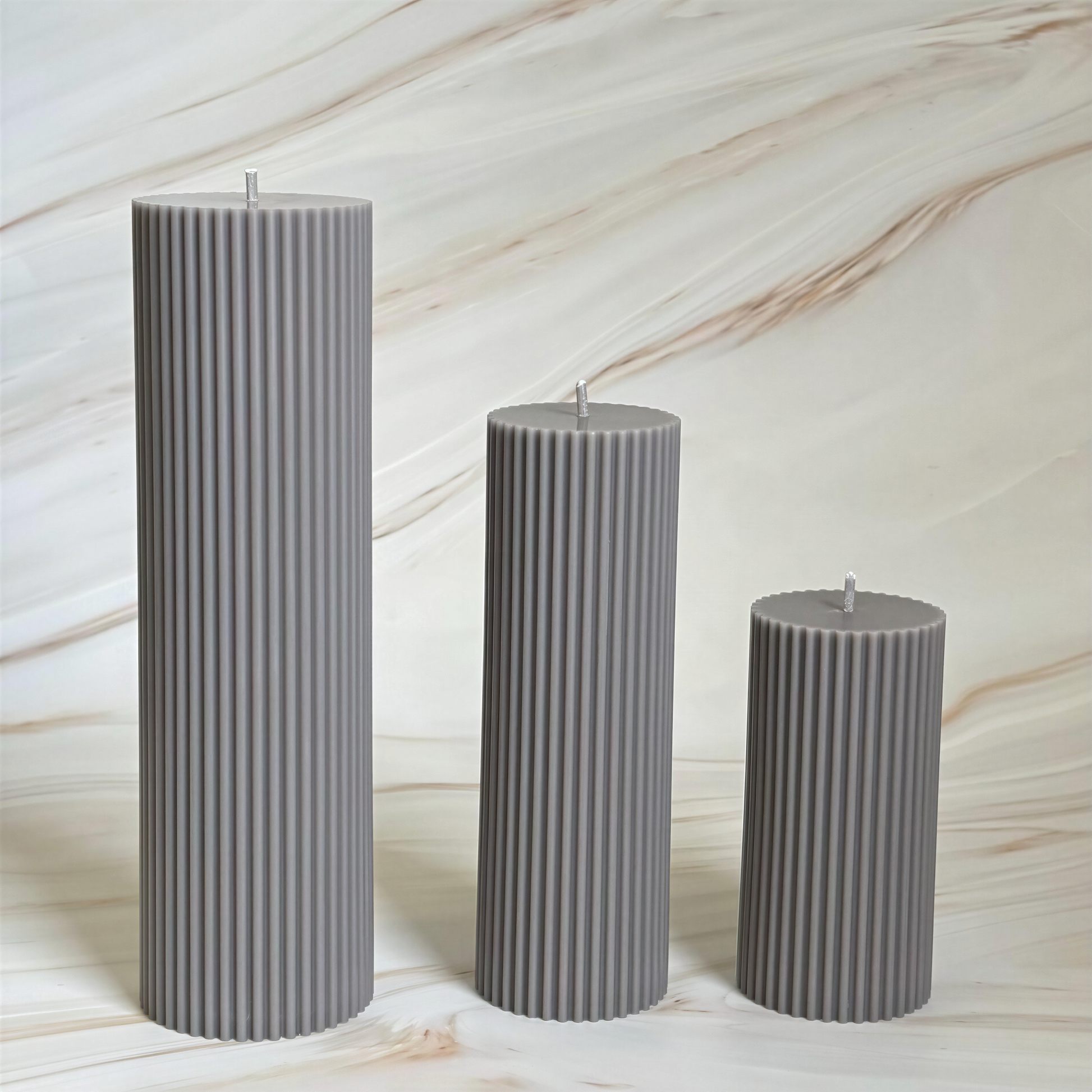 Three gray cylindrical candles are arranged in a row against a marble background.