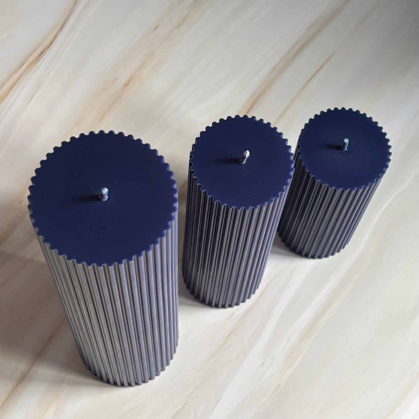 Three cylindrical candles with blue lids are arranged in a row on a marble surface.