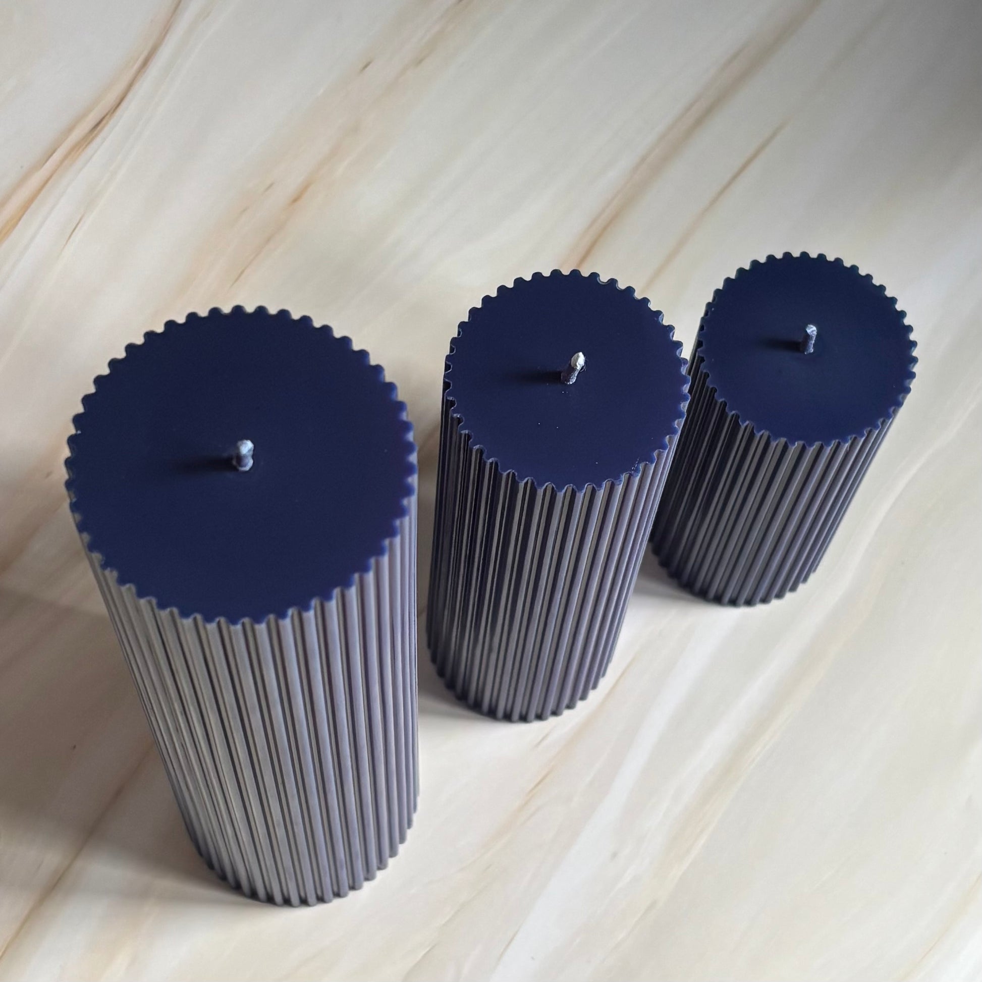Three cylindrical candles with blue lids are arranged in a row on a marble surface.