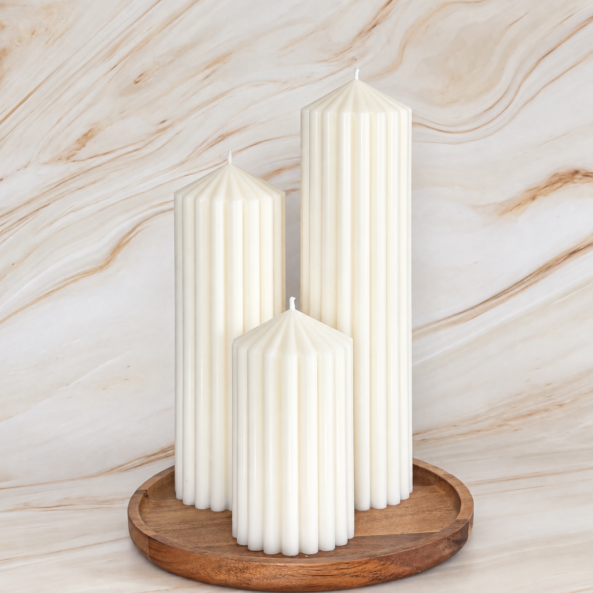 Three tall white candles with a cylindrical shape and a pointed top are displayed on a wooden tray against a marble background.