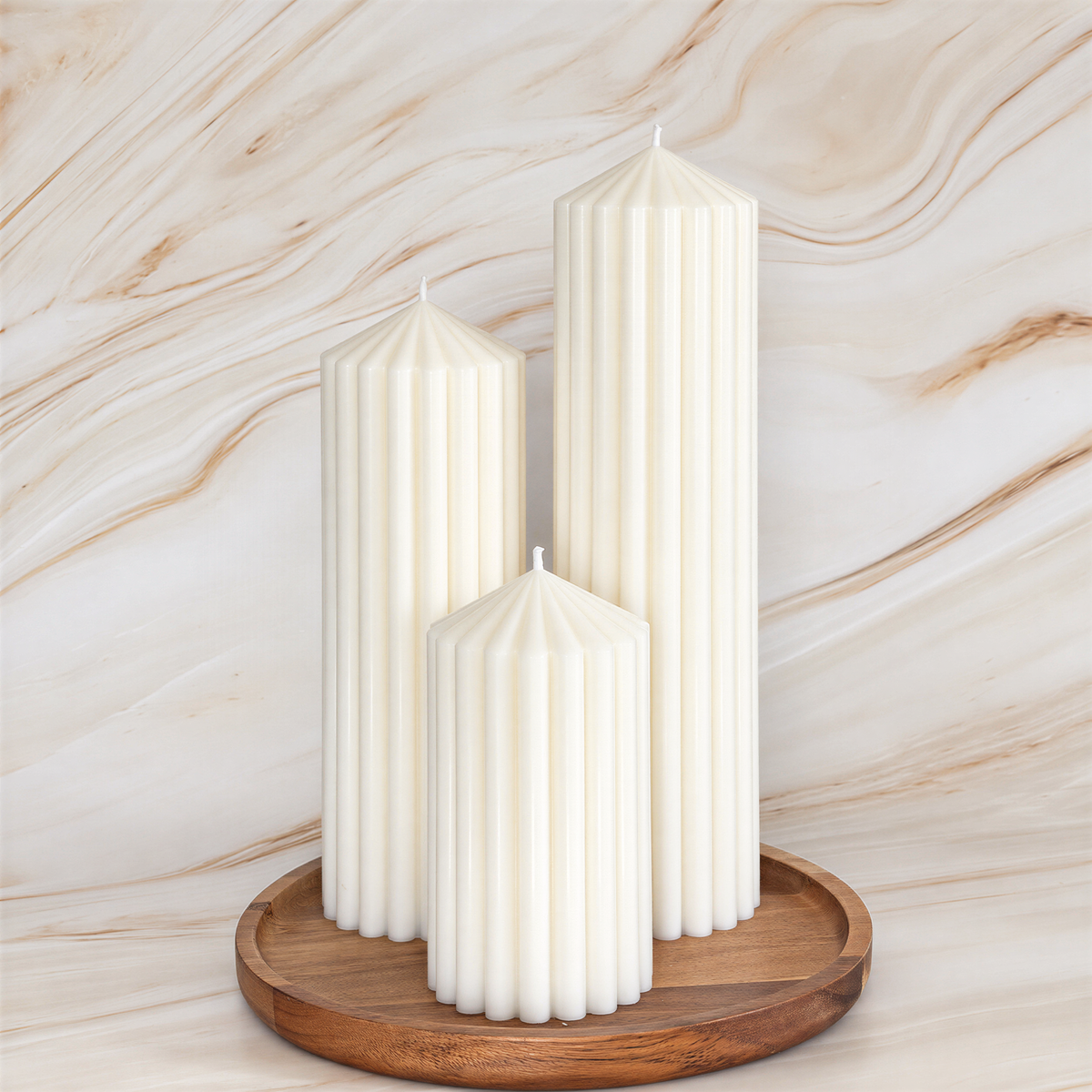 Three tall white candles with a cylindrical shape and a pointed top are displayed on a wooden tray against a marble background.