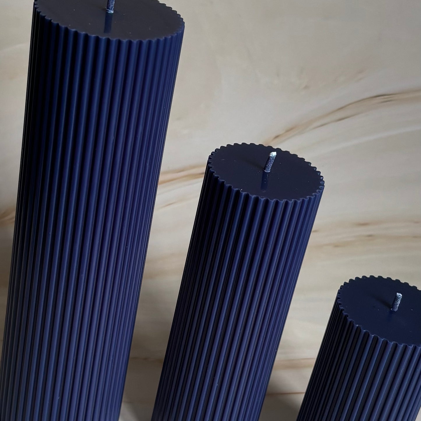 Three tall, cylindrical candles in a dark blue color, arranged in a row.