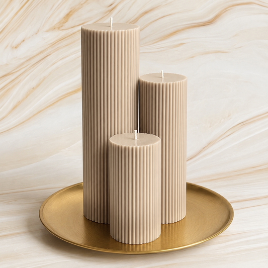 Three beige pillar candles with a golden plate underneath them, set against a marble-like background.