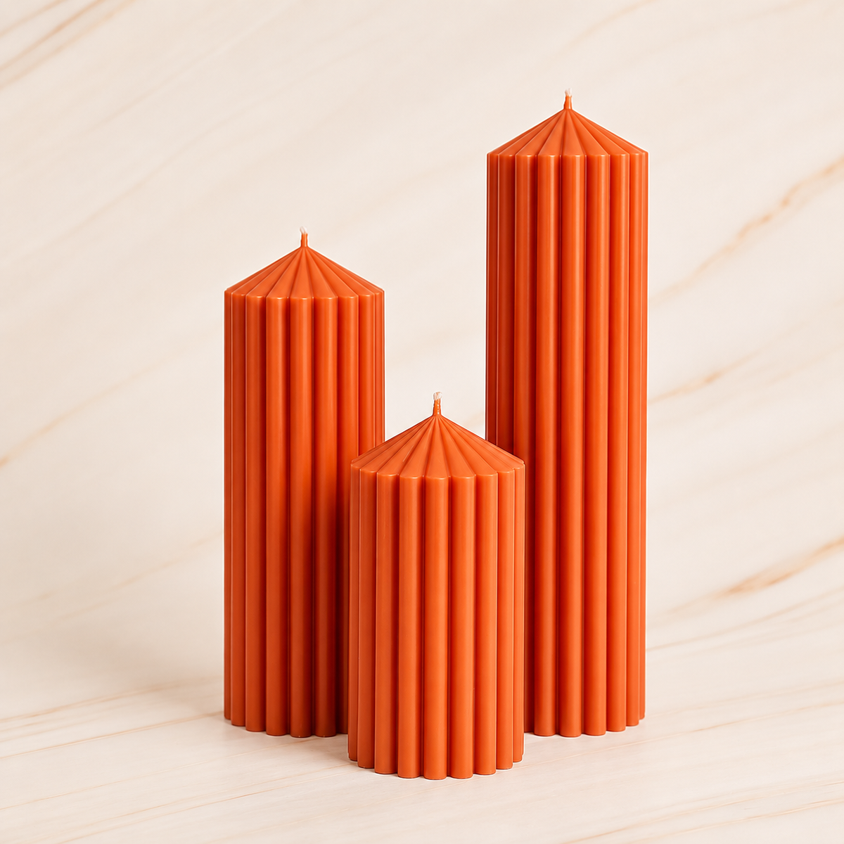 Three tall orange candles with pointed tops are arranged in a row against a light-colored marble background.