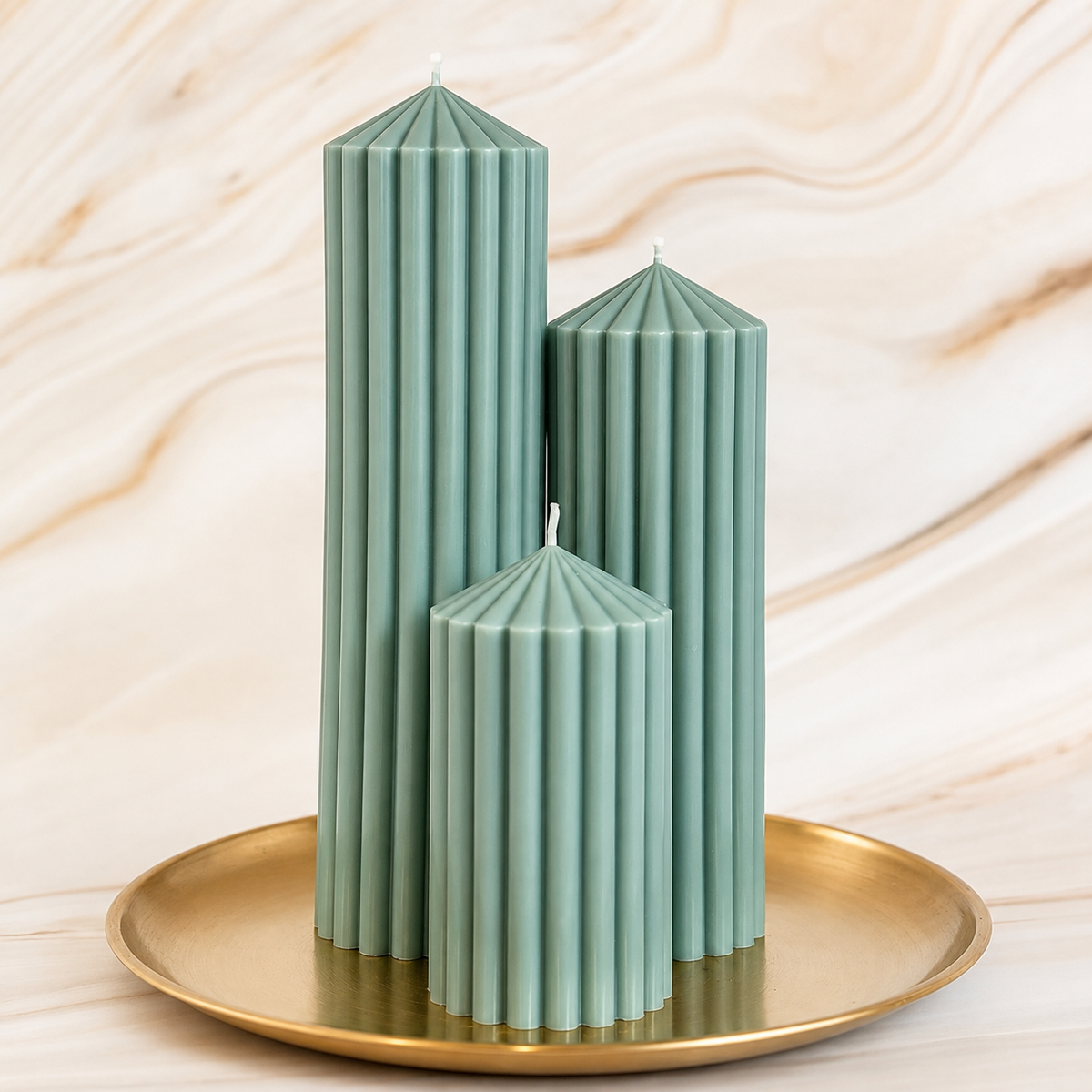 Three tall, green candles with ribbed surfaces are displayed on a gold tray against a marble background.