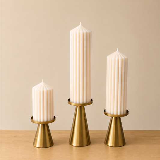 Three tall, white candles with gold bases are arranged in a row on a wooden surface against a beige background.