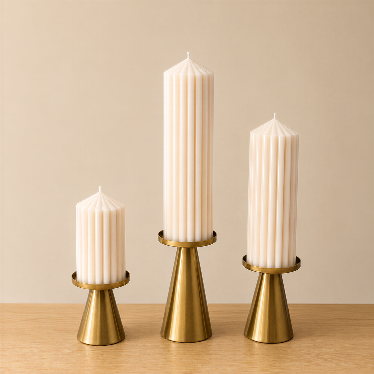 Three tall, white candles with gold bases are arranged in a row on a wooden surface against a beige background.
