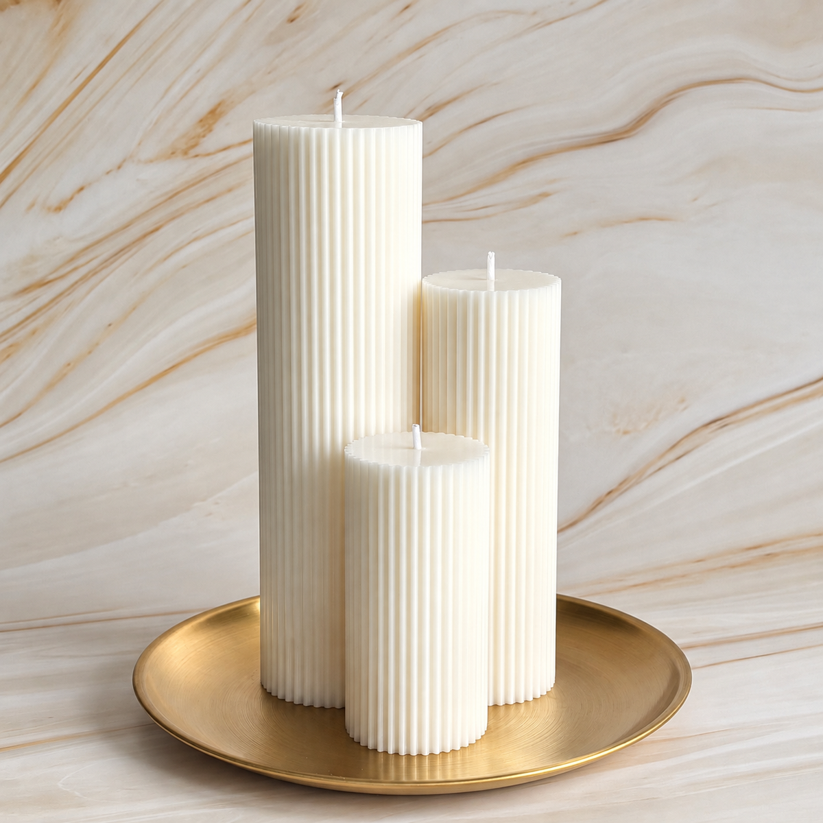 Three white pillar candles are displayed on a gold plate against a marble background.