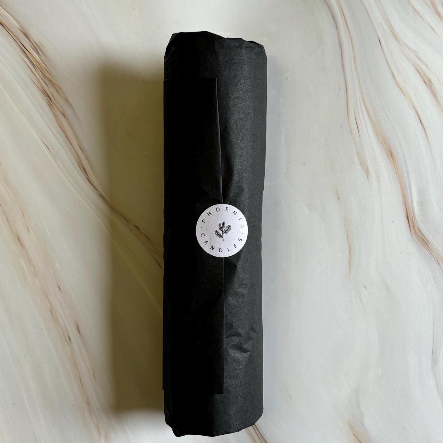 A black cylindrical object wrapped in black paper, with a white circular label on it, placed on a marble surface.