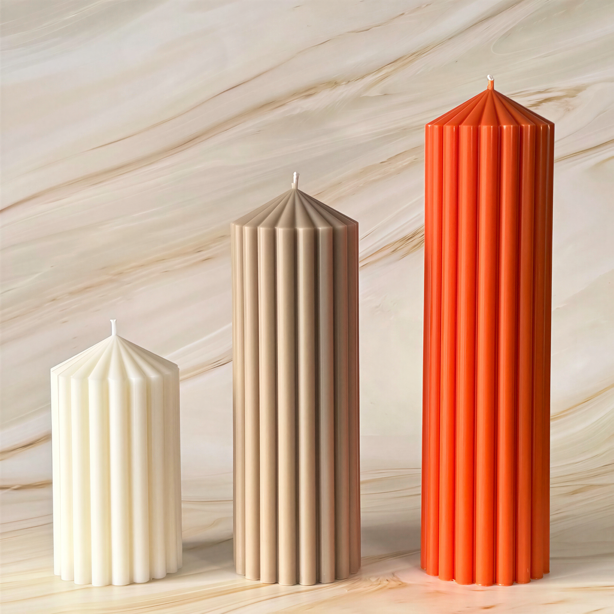Three tall candles of different colors - white, beige, and orange - stand upright against a marble background.
