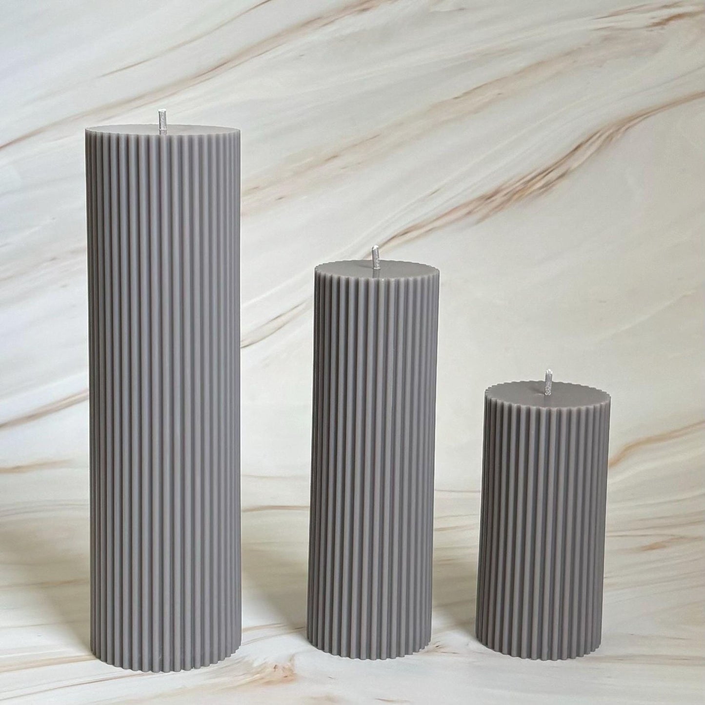 Three gray cylindrical candles with a textured appearance stand in a row against a marble-like background.